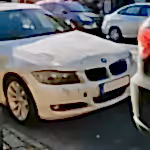 White BMW sedan with front-end damage parked on a busy city street.